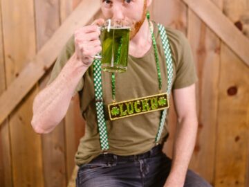 Caucasian man in green attire enjoying St. Patrick's Day with a mug of green beer and festive costume.
