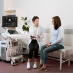 Healthcare professional consulting with a pregnant patient in a medical clinic using ultrasound equipment.