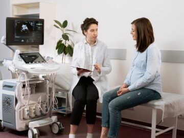 Healthcare professional consulting with a pregnant patient in a medical clinic using ultrasound equipment.