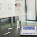 Tablet displaying digital voter registration at indoor voting station with vote day signs.