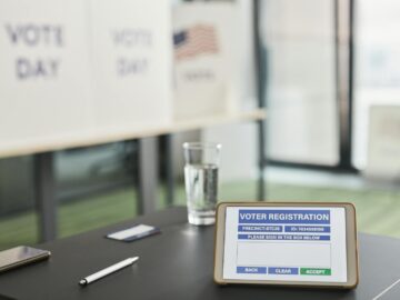 Tablet displaying digital voter registration at indoor voting station with vote day signs.