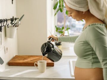 Expectant mother pouring tea in the kitchen with a towel on her head, creating a warm morning scene.
