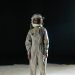 Astronaut standing in spacesuit on moon-like surface with black background.