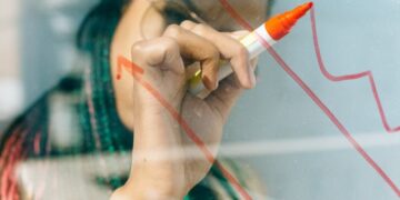A businesswoman draws a red financial graph on a glass panel, symbolizing strategy and success.