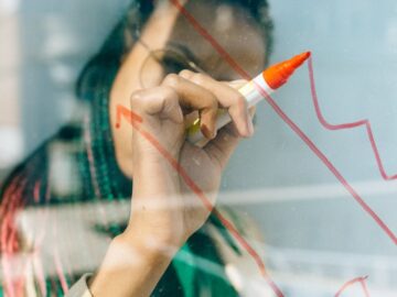 A businesswoman draws a red financial graph on a glass panel, symbolizing strategy and success.