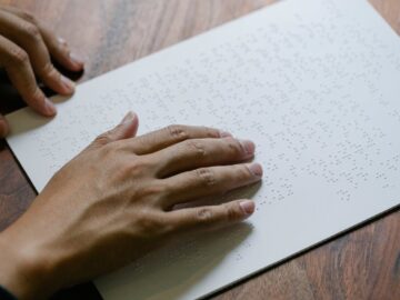 Hands gently read a Braille text sheet providing tactile learning experience.