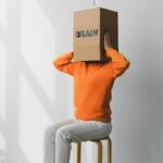 Crop anonymous person putting creased paper with Rubbish inscription in container with Brain title on head of female on chair