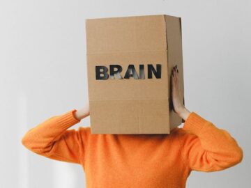 A person wears a box labeled 'brain' while discarding 'rubbish' paper, symbolizing mental clutter.