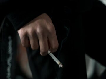 A close-up shot of a person holding a lit cigarette, depicting smoking habit indoors.