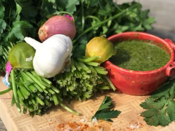 A vibrant collection of fresh herbs and ingredients including parsley, garlic, limes, and sauce displayed on a cutting board.