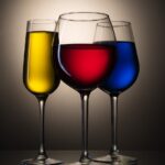 Close-up of three cocktail glasses filled with yellow, red, and blue liquids against a warm backdrop.