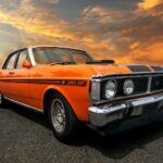 Vintage orange Ford Falcon 351 GT muscle car shining against a vibrant sunset sky.