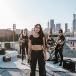 A stylish band playing music on a rooftop with city skyline in the background.