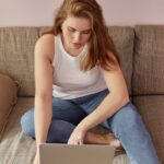 Woman in casual attire using a laptop on a couch, representing remote work lifestyle.