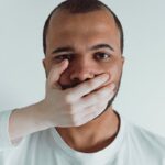 Conceptual close-up of a man with a hand covering his mouth, symbolizing silence or restraint.