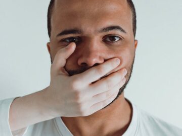Conceptual close-up of a man with a hand covering his mouth, symbolizing silence or restraint.