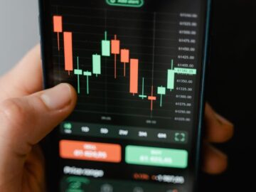 Hand holding smartphone displaying cryptocurrency trading graph in app.