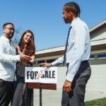 A couple meets with a realtor to finalize the purchase of their new home, indicated by a 'Sold' sign.