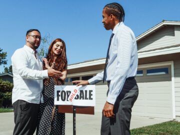 A couple meets with a realtor to finalize the purchase of their new home, indicated by a 'Sold' sign.