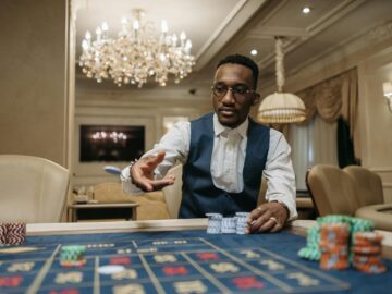 A man in formal attire plays roulette in a luxurious casino under a chandelier.