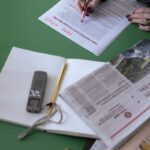An overhead view of a person editing newspapers and documents at a desk.