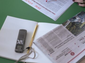An overhead view of a person editing newspapers and documents at a desk.
