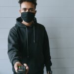 A masked man offering a wireless payment terminal, symbolizing contactless transactions and safety.