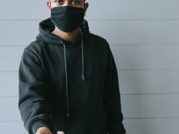 A masked man offering a wireless payment terminal, symbolizing contactless transactions and safety.