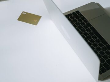 A laptop with a credit card, surrounded by paper bags, illustrating online shopping.