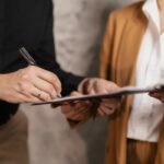 Close-up of two professionals signing a business document, emphasizing collaboration and negotiation.