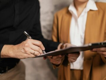 Close-up of two professionals signing a document indoors, focus on hands and pen.