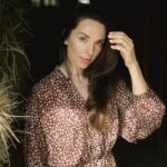 Elegant woman in floral dress standing near hay in a farm setting.