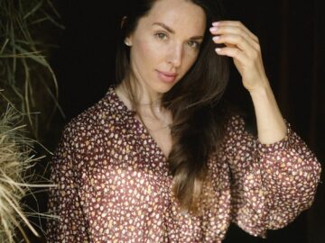 Elegant woman in floral dress standing near hay in a farm setting.