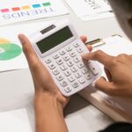 Close-up of a person's hand using a calculator on a desk with financial documents.