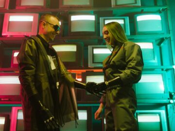 Futuristic scene of two adults shaking hands with prosthetics against a retro TV backdrop.