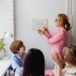 A teacher in a pink blazer interacts with students during a classroom session labeled 'Back to School'.