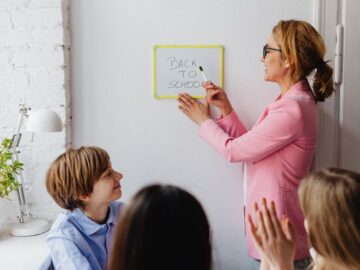 A teacher in a pink blazer interacts with students during a classroom session labeled 'Back to School'.