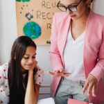 Female teacher assisting teenage girl with homework in classroom setting.
