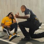 A police officer interacts with a man in a yellow shirt in a parking lot.