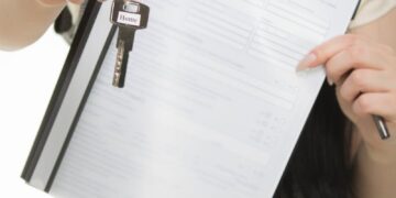 Close-up of person holding home insurance document and house key, symbolizing real estate and security.