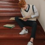 Young man reading on stairs with books, embodying study and focus in a school environment.