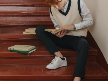 Young man reading on stairs with books, embodying study and focus in a school environment.