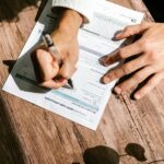 Hands writing on a consumer loan credit application form on a wooden table.