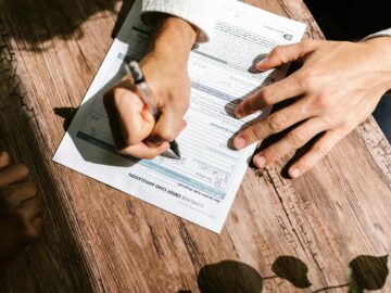 Hands writing on a consumer loan credit application form on a wooden table.