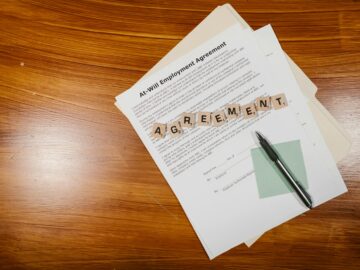 A flat lay of an employment agreement with Scrabble tiles on a wooden table.
