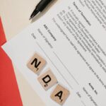 NDA document on table with Scrabble tiles and pen in office setting.