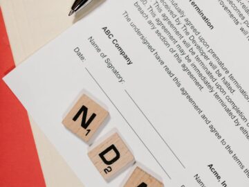 NDA document on table with Scrabble tiles and pen in office setting.