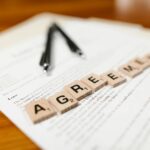 Scrabble tiles spelling 'AGREEMENT' on a lease document, emphasizing contractual themes.