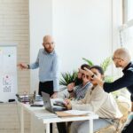 A group of professionals engaged in a business meeting, discussing financial graphs on a whiteboard.