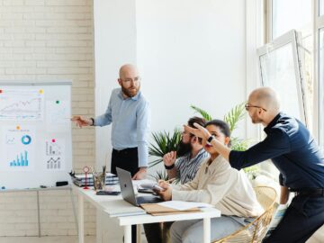A group of professionals engaged in a business meeting, discussing financial graphs on a whiteboard.